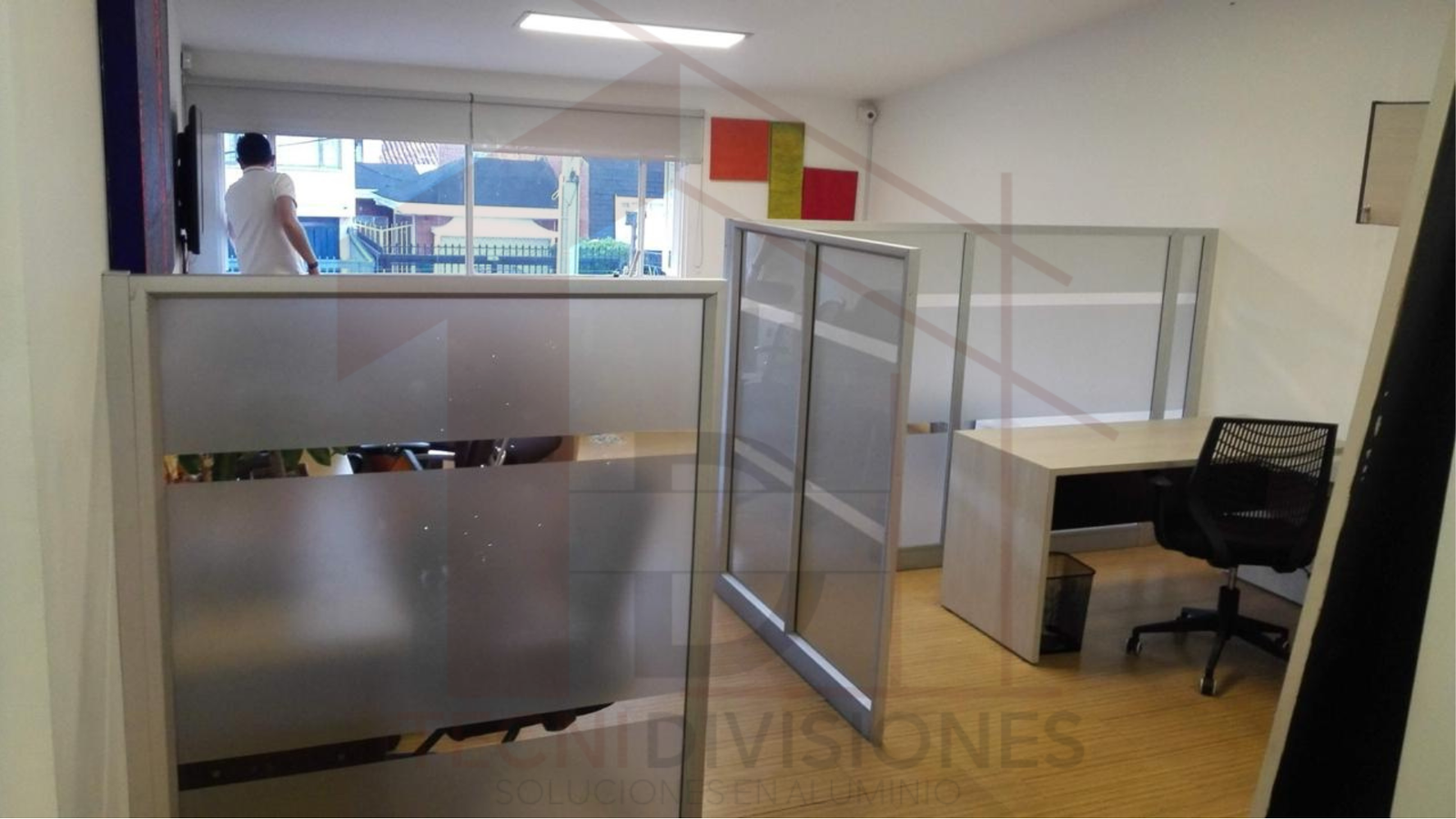 Cubículos de oficina con divisiones a media altura en vidrio y aluminio, con un estilo funcional y minimalista